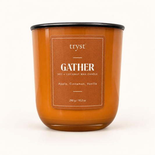 Gather soy and coconut wax candle in an orange glass jar with a black lid, labeled apple, cinnamon, vanilla