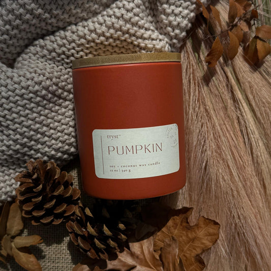 Candle labeled 'Pumpkin' with autumn decorations on a textured surface