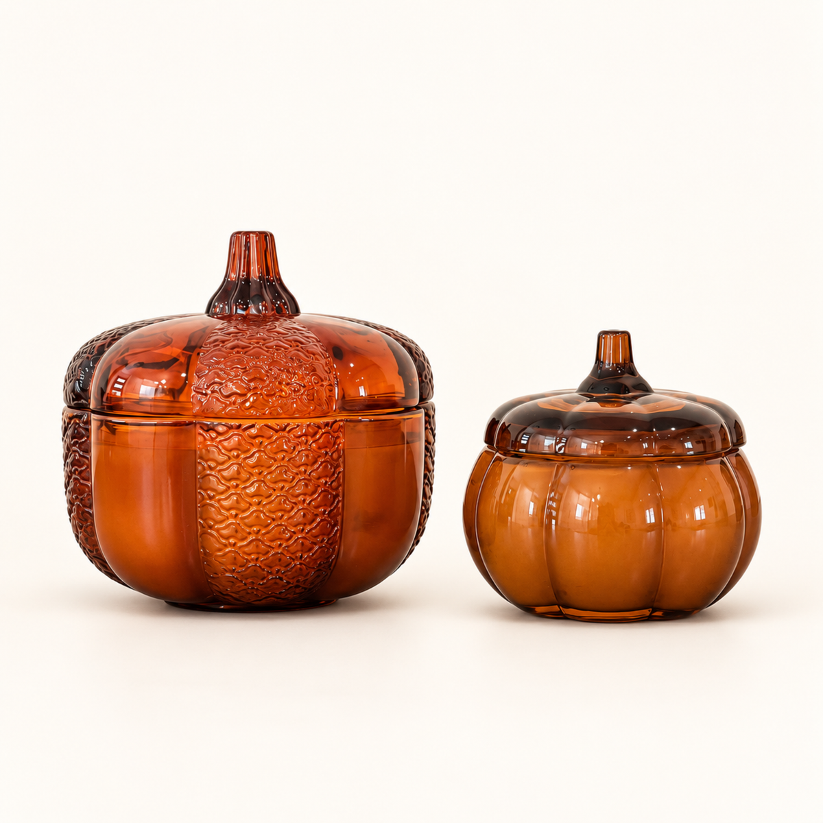 Large and small Pumpkin candles side by side in amber glass pumpkin-shaped jars with stem-handled lids