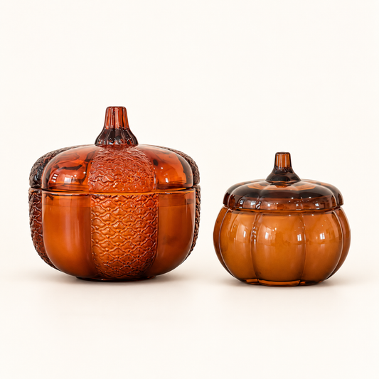 Large and small Pumpkin candles side by side in amber glass pumpkin-shaped jars with stem-handled lids